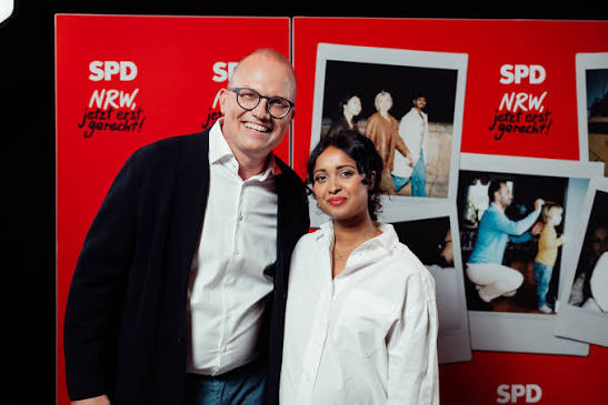 Roshani Thanapalasingham zusammen mit einem Mann vor einer roten SPD-NRW-Wand