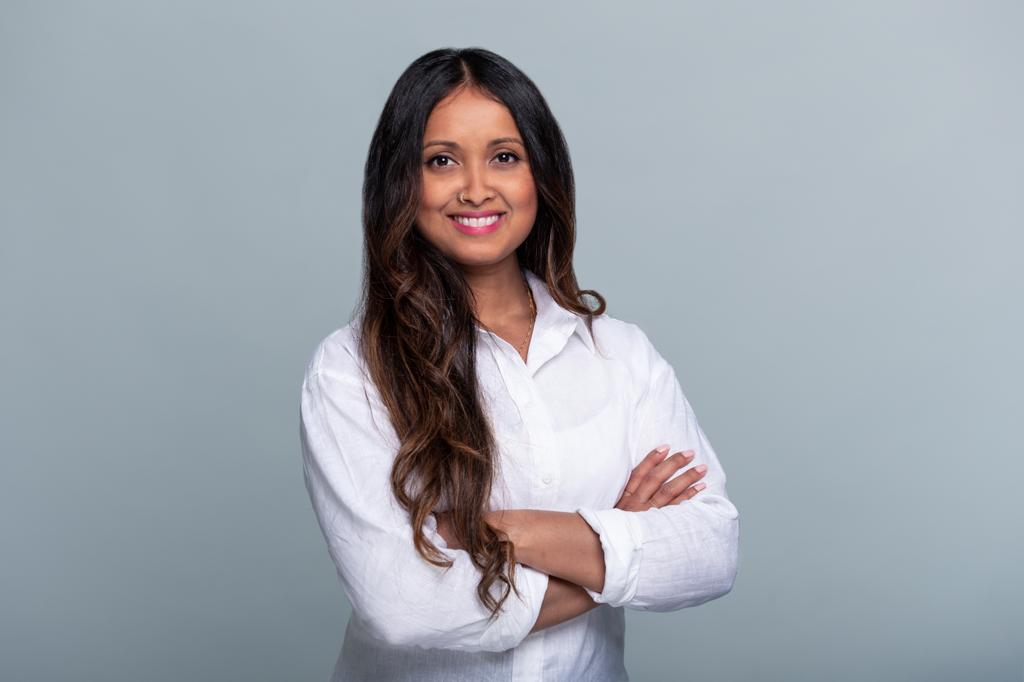 Roshani Thanapalasingham im Porträt, in weißer Bluse mit verschränkten Armen