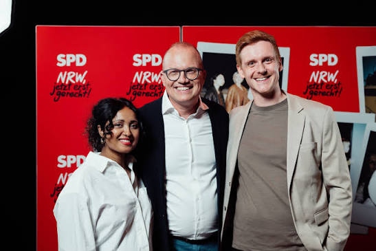 Roshani Thanapalasingham mit zwei Männern vor einer roten SPD-NRW-Wand